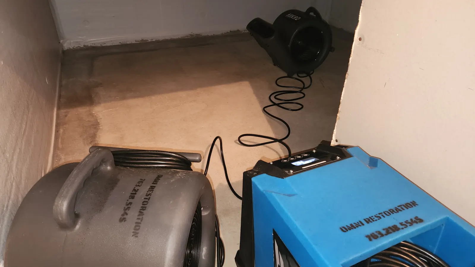 Omni Restoration air movers and dehumidifier drying a basement storage area with water staining on the concrete floor